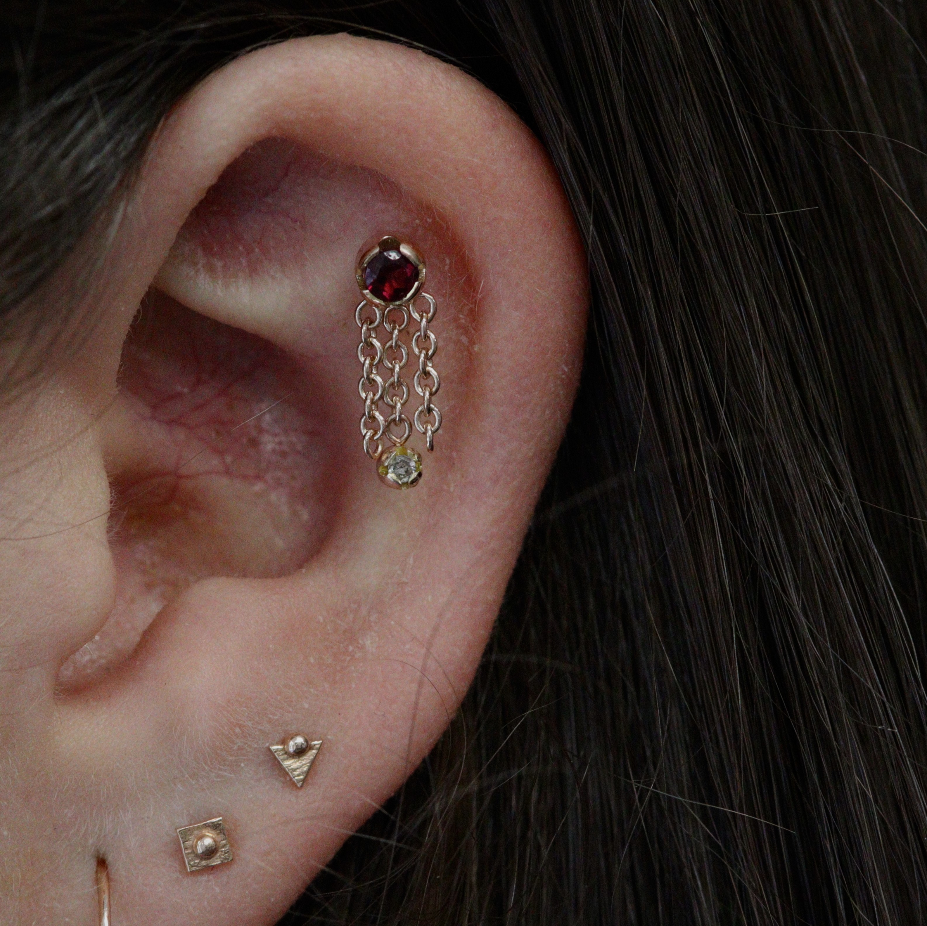 Helix flat piercing with bespoke piece from Ixus Fine Jewellery in 18k yellow gold with garnet and moissanite